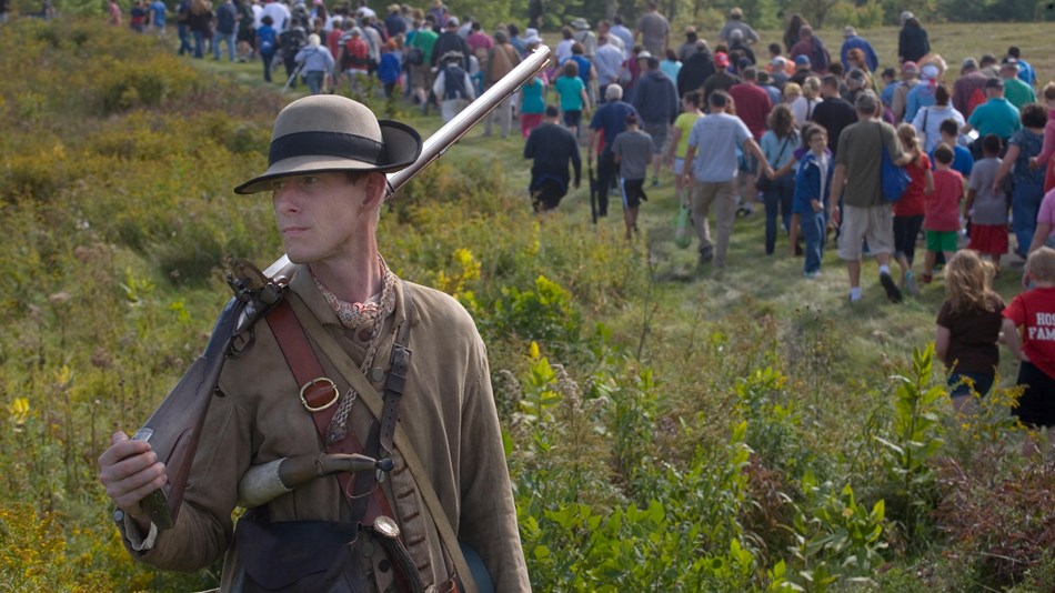 Revolutionary Soldier in foreground with visitors hiking in background