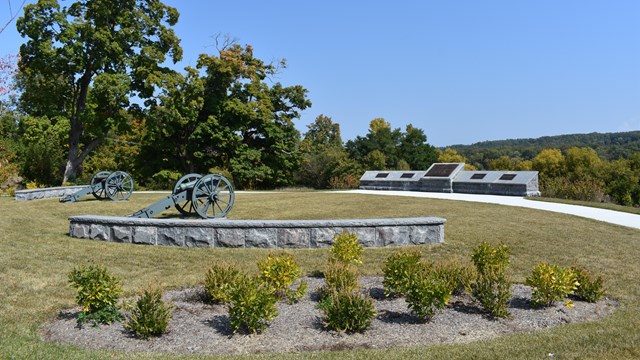 A grassy area surrounded by a stone wall, encompassing two canons.