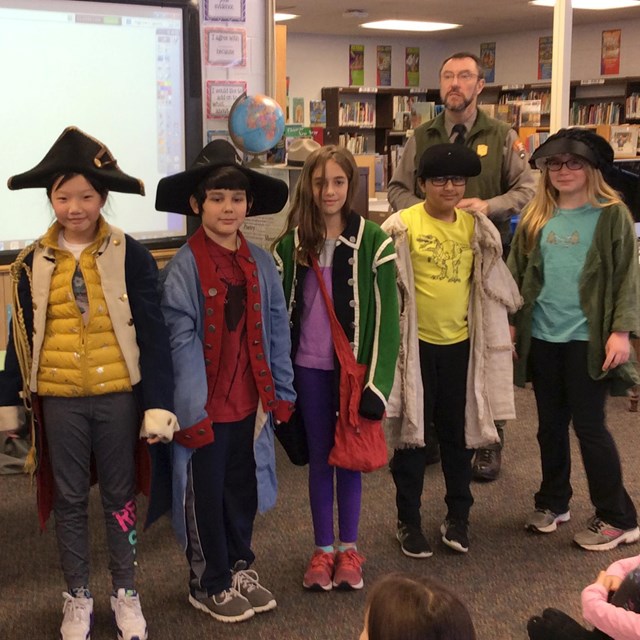 A park ranger stand with students dressed in 18th century clothing.