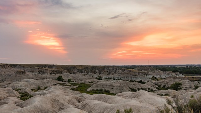The sun sets over a series of undulating badlands formations