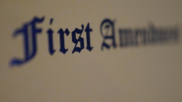 A yellow sign has text that is partially out of focus, but appears to read First Amendment. 