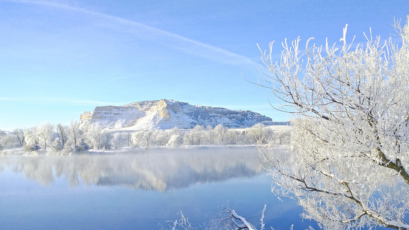 A sandstone bluff and trees with golden leaves are reflected in the waters of a pond.