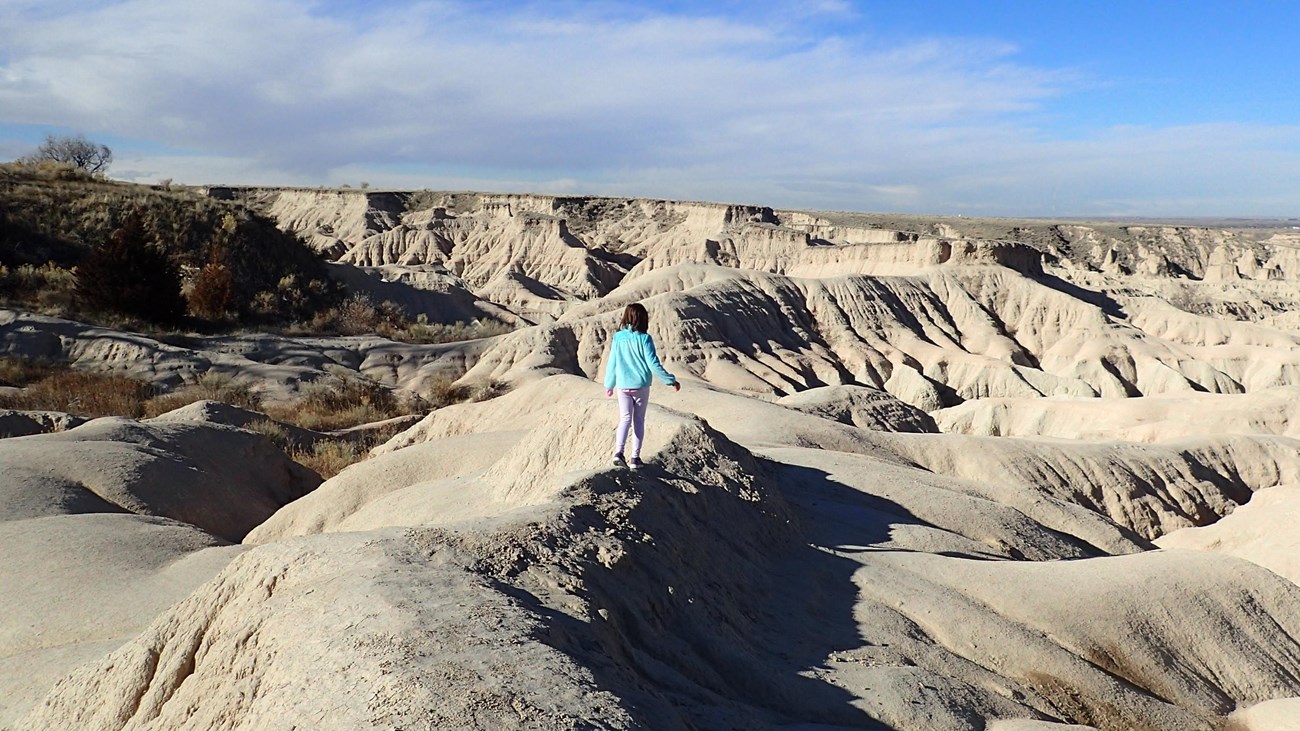 A girl stands in an eroded landscape of badlands formations. 