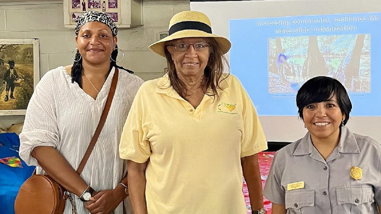 Three smiling women of color, one in National Park Service uniform, pose for a photo