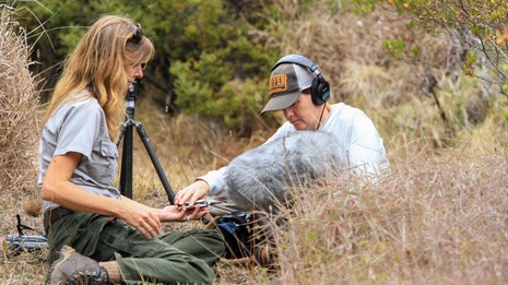 a female ranger sits with an audio technician in tall grass