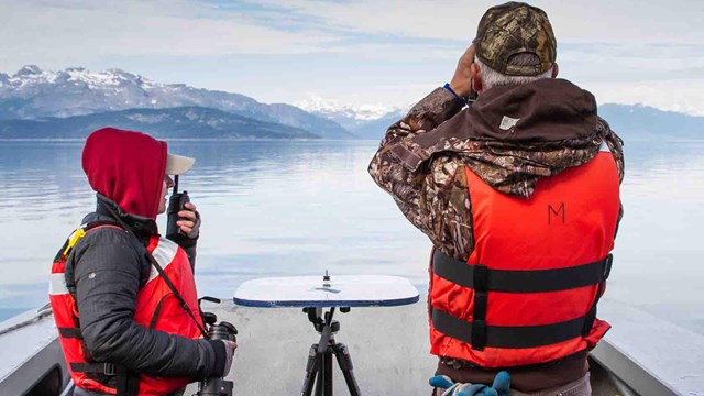 Two researchers on a boat watching the sea with binoculars.