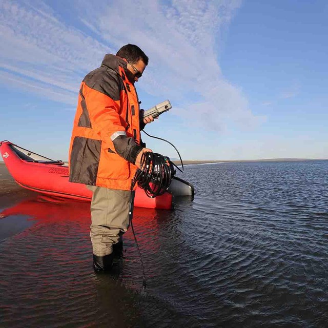A researcher collects data in a lagoon with an inflatable boat behind him.