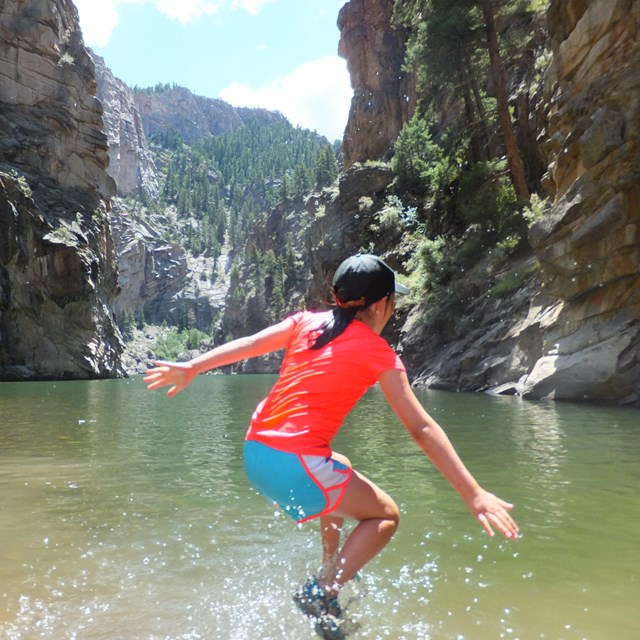 Girl jumps into water at the bottom of a steep-walled canyon.