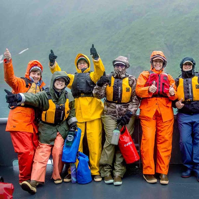 A group of teachers at the bow of a research vessel wearing bright-colored rain gear.