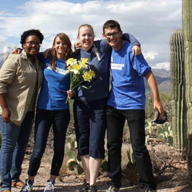 A group of youth pose by a saguaro.