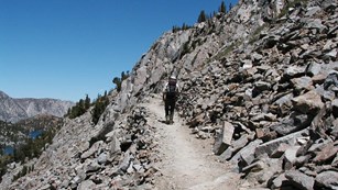 A hiker climbs a trail along a rocky slope
