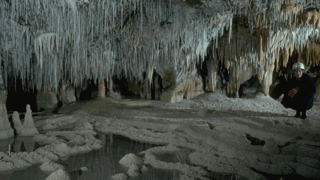 Cave specialist standing in amidst icy-colored cave formations. 