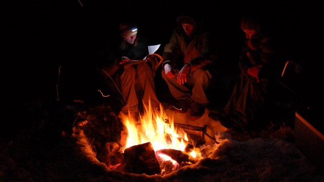 A group of campers relaxing around a fire.