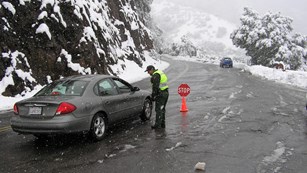 A ranger talks with a driver on a snowy roadway