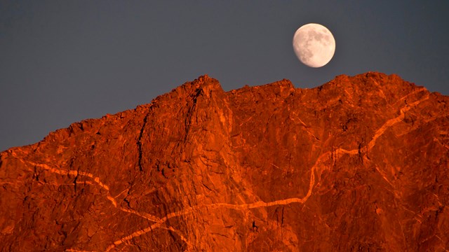 A moonrise over reddish peaks