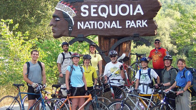 People with bicycles pose in front of the park entrance sign