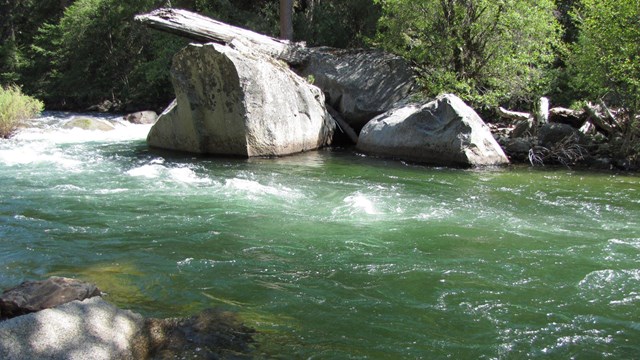 Deep blue-green colored river flows past granite boulders.