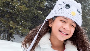 A young girl with a white cat hat and white coat smiles. Photo by Alison Taggart Barone