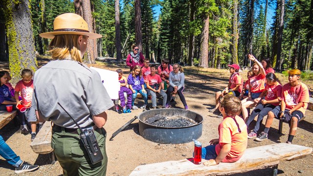 A park ranger speaks to a group of children, one of whom has their hand raised. 