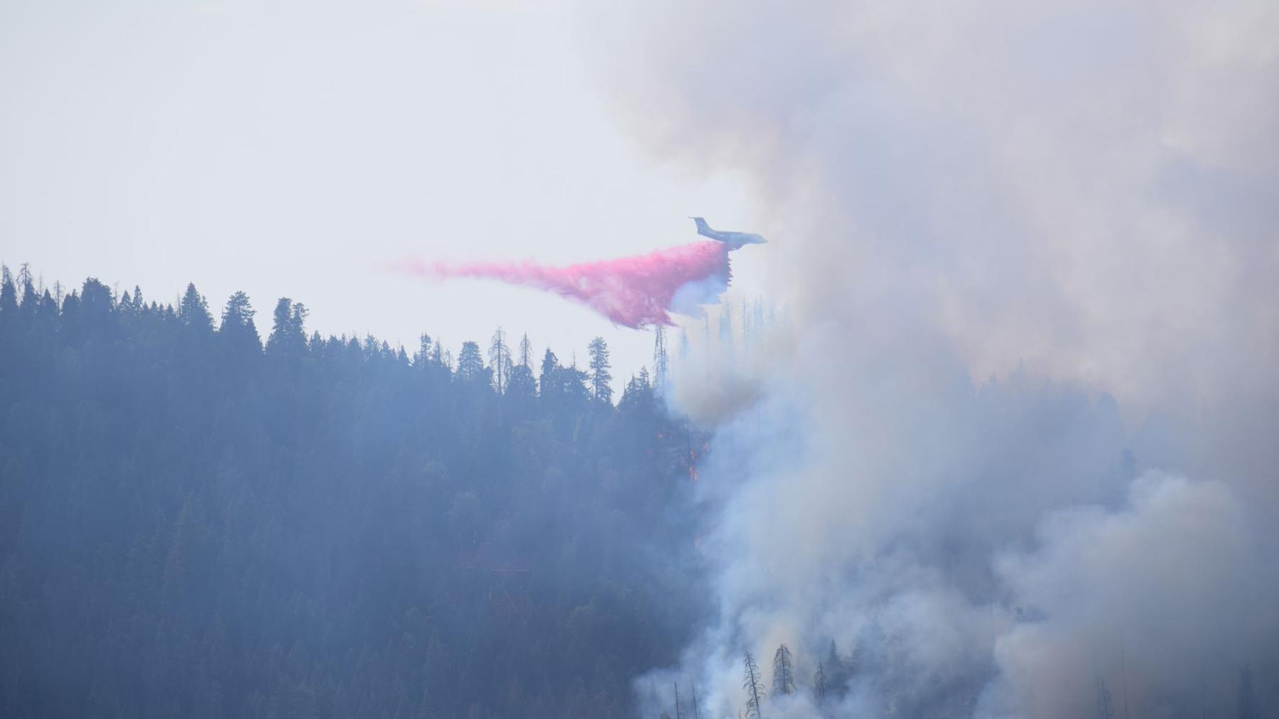 A plane drops red fire retardant onto the smoking forest below.
