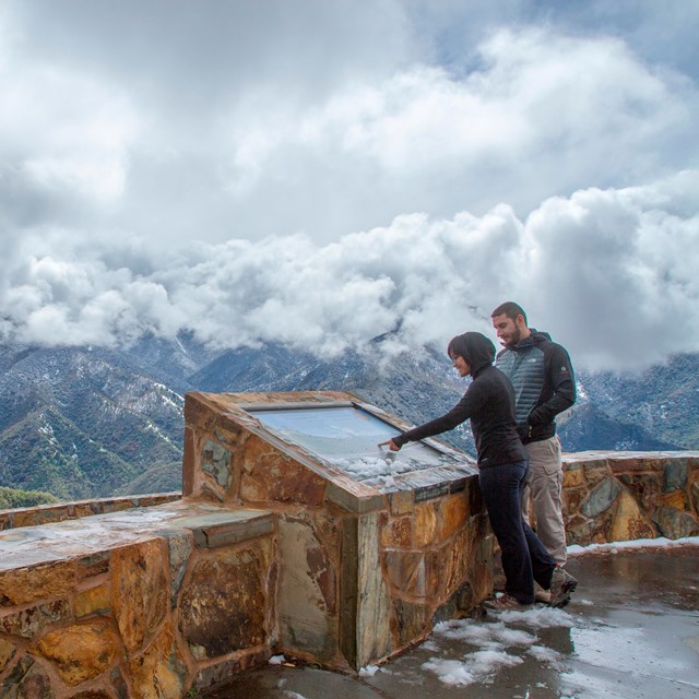 People read an exhibit at a snowy viewpoint. Photo by Kirke Wrench.