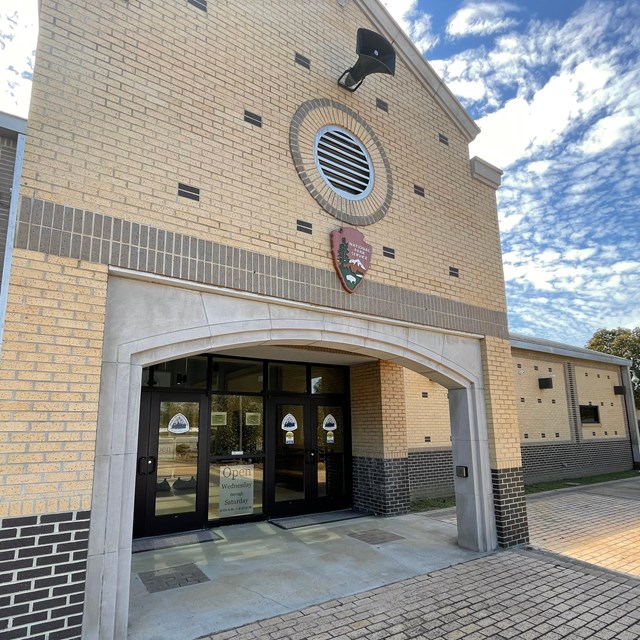 View looking upwards at a tall tan brick building with a National Park Service logo.