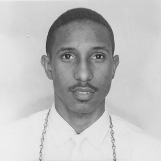Black and white photo of a young black man standing for a police mug shot.