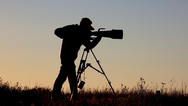 A silhouette of a man with a video camera in a meadow.
