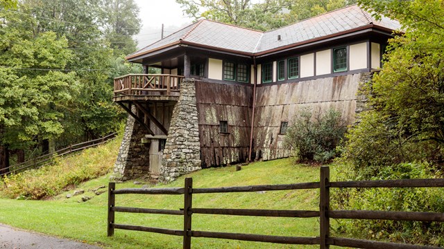 A split rail fence leads to an old, historic building with wood shingle siding and a balcony.