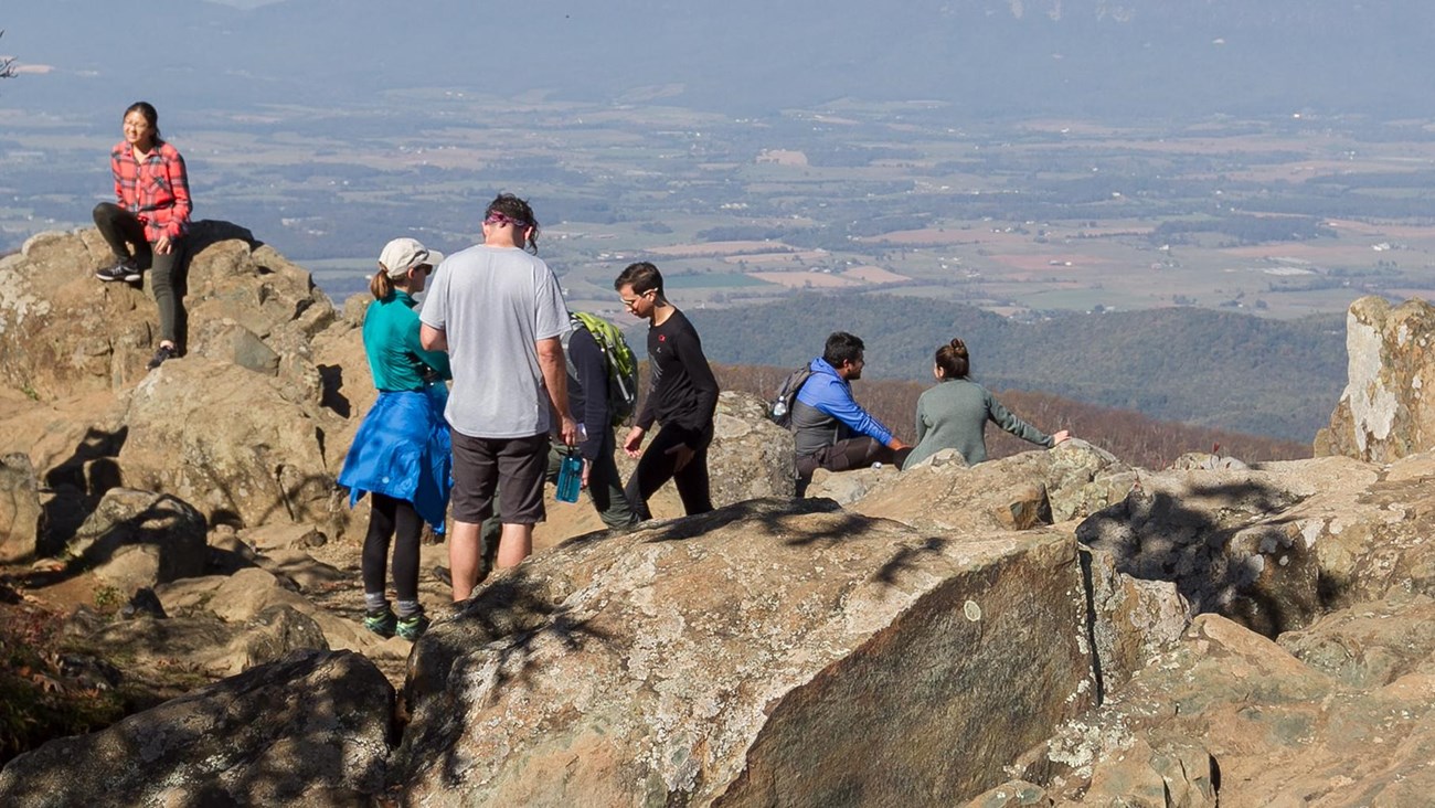 People recreating on a rock outcrop overlooking a valley below.