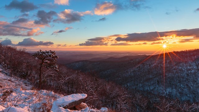 A sunrise behind a mountain layer covered with snow.