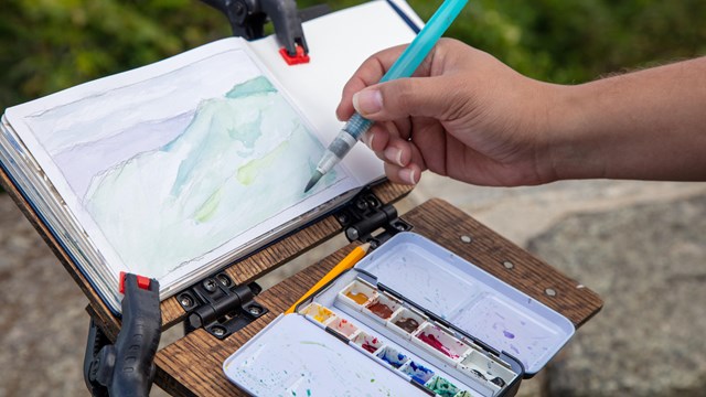Watercolor paint setup for postcard art of a mountain landscape. 