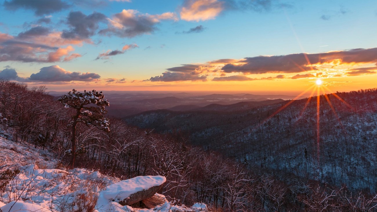 A sunrise behind a mountain layer covered with snow.