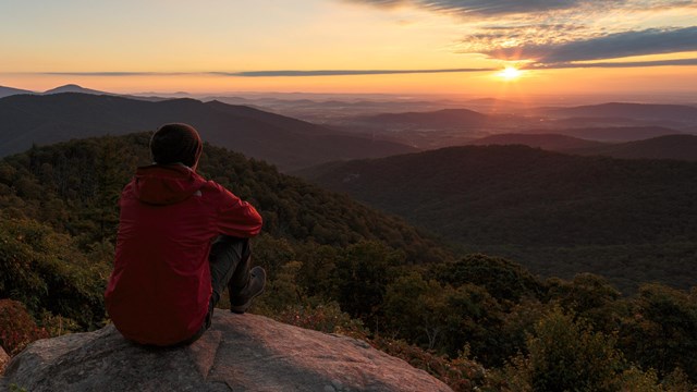 A man sitting on a rock looking out over mountains and a valley .