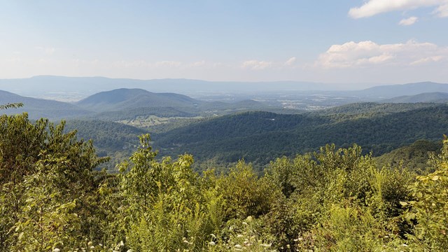 A view from an overlook on a mountain looking into a valley with foothills in the distance.