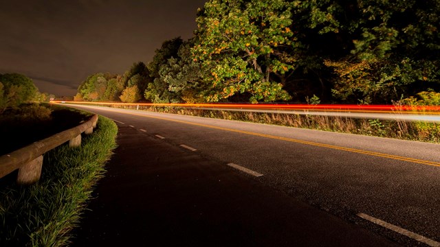 A road at night with the light trails of a car speeding through the image.