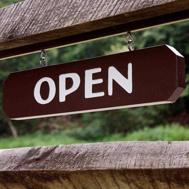 A brown open sign hanging from a wooden fence.