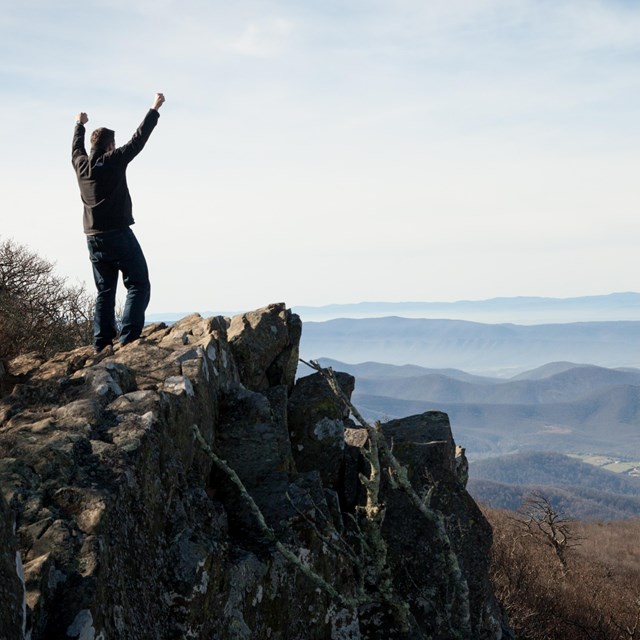 A man stands at the peak of hawksbill mountain. 