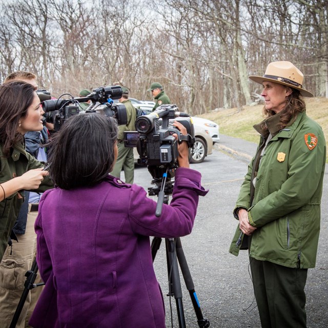 A female park employee stands calmly in front of a group of reporters with video cameras.