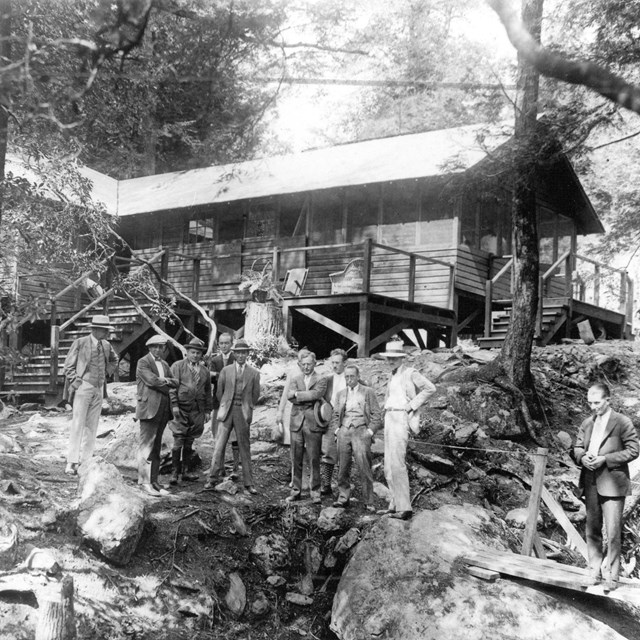 A black and white image of a group of reporters standing outside of a rustic building, Camp Hoover.