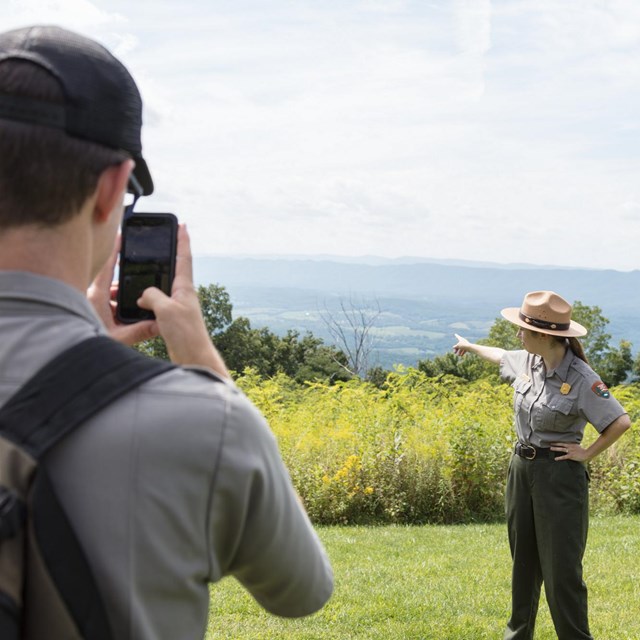 A park ranger takes a picture of another park ranger with their cell phone.