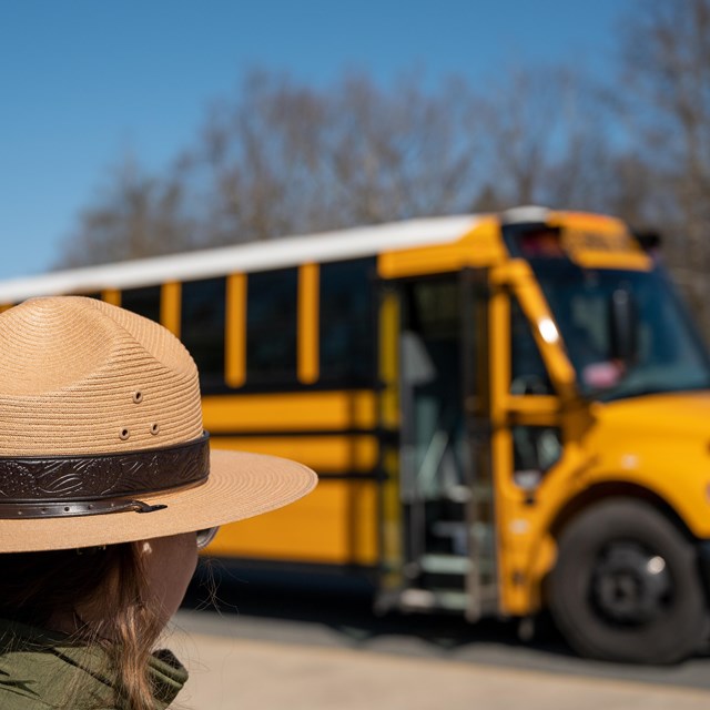 Ranger wearing a flat hat standing in front of a yellow school bus