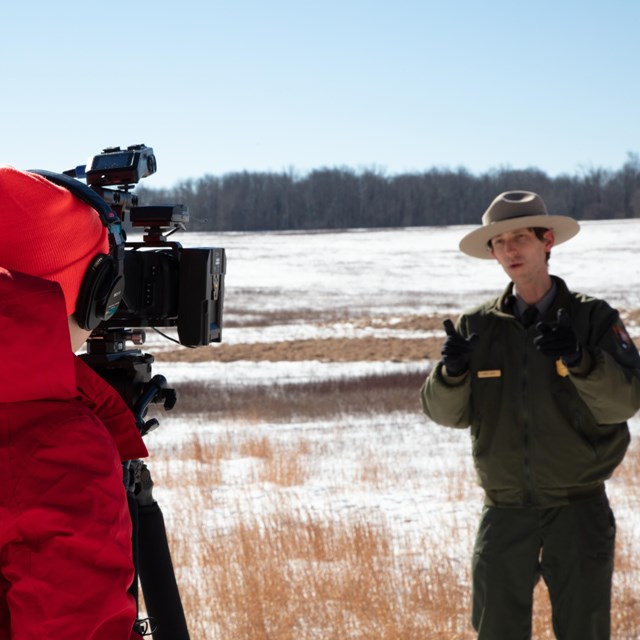 A ranger being filmed doing a virtual ranger program with a snowy meadow backdrop