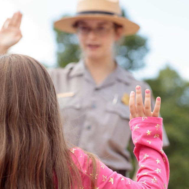 A park ranger swears in a Junior Ranger, whose hand is raised to take an oath.