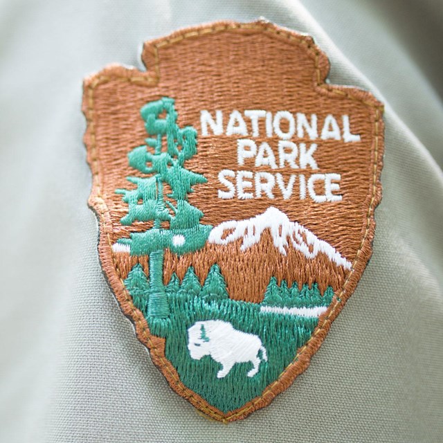 A close up of the National Park Service arrowhead patch on a park ranger's uniform.