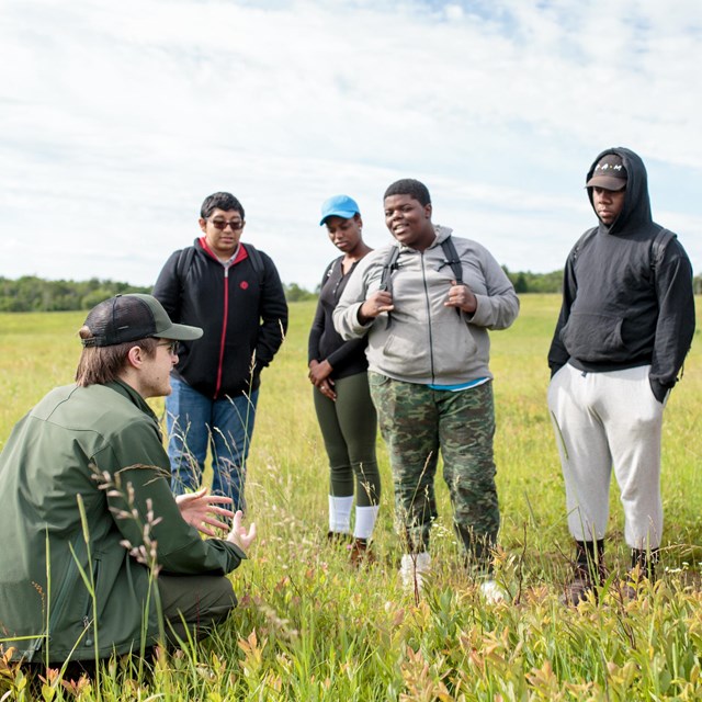 A group of teenage students listen to an education Ranger amongst  the plants of Big Meadows.
