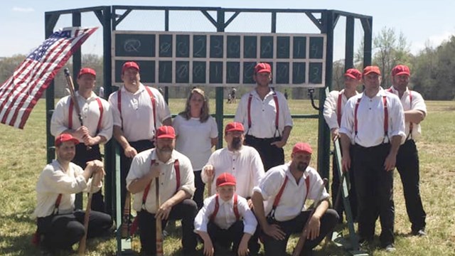 Living historians in period base ball uniforms pose in front of a backstop