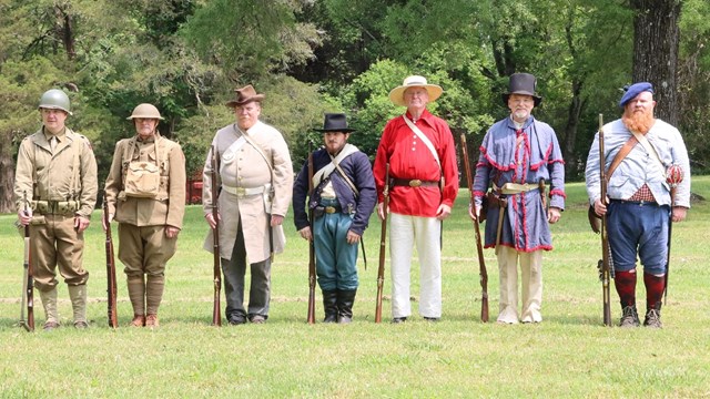 Living historians in period military uniforms stand at attention. 