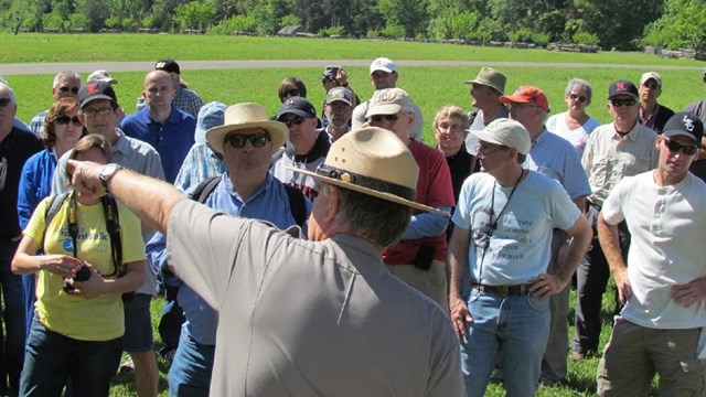 Park Ranger in green and gray pointing to a crowd. 
