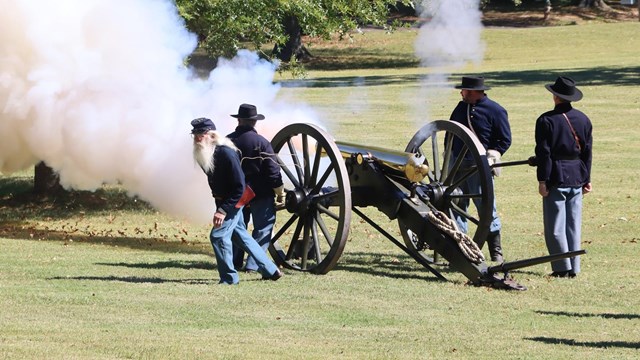 Living historians in blue uniforms fire a bronze cannon. 